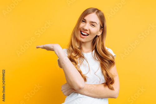 Portrait of a happy girl showing her hand on an empty copy space on a yellow background.