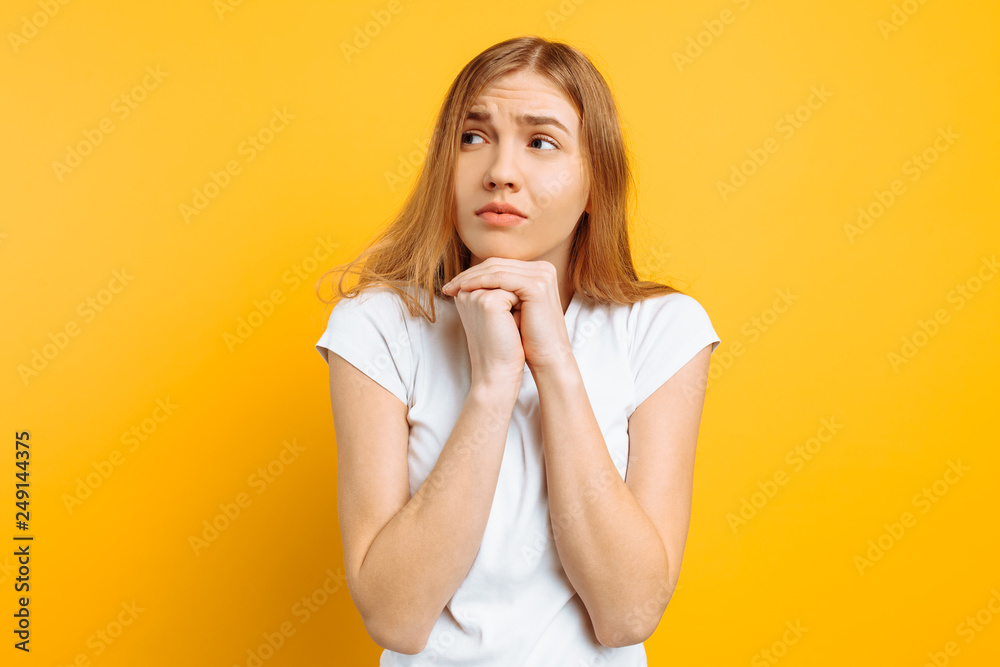 The excited girl is frightened by something, bites her nails, has a restless facial expression, stands on a yellow background, The excited girl is frightened by something, bites her nails, has a restless facial expression, stands on a yellow background,