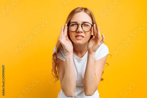 A girl with poor eyesight wears glasses, looking squinting, trying to figure out what is written on a yellow background photo