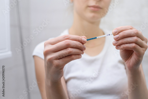 A young attractive woman holds a pregnancy test in her hand. The girl is shocked by the positive result of the pregnancy test. Unwanted pregnancy