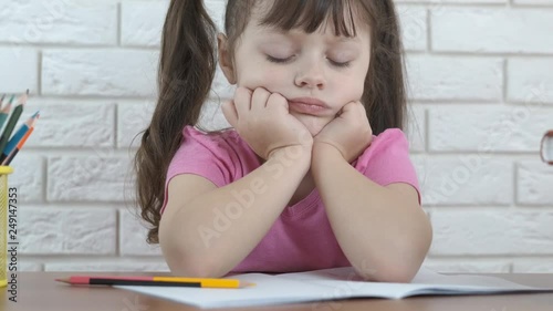 Sad child doing homework. A cute little girl looks at a school notebook. Child learning difficulties concept.