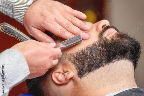 Handsome man having a shave with vintage razor at the barbershop .