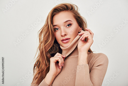 In her own style. Attractive young woman holding collar of beige turtleneck near her face, isolated over white background photo