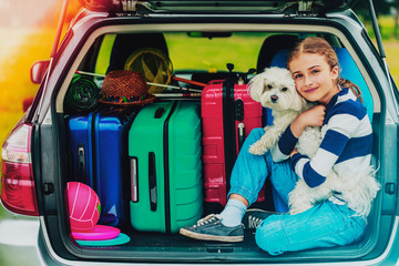 Summer vacation, young girl in car trunk with dog in the car is ready for travel for family vacation.