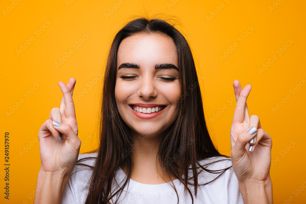 Amazing caucasian woman making a wish with crossed fingers and cheches teeth in front of a yellow background. I really want to win. Amazing caucasian woman making a wish with crossed fingers and cheches teeth in front of a yellow background. I really want to win.
