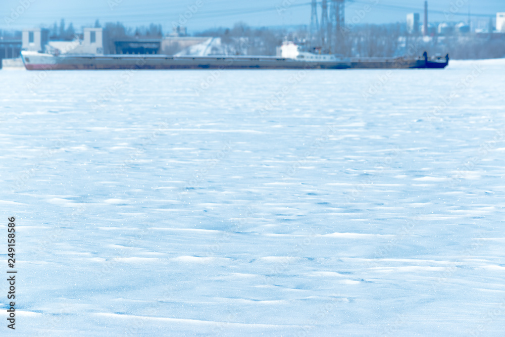 View of snow covered frozen river on a bokeh background of barge in ice. Selective focus
