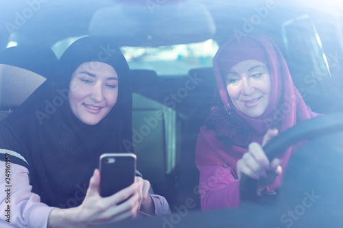Two Muslim women travelling in the car, looking the way at the smartphone