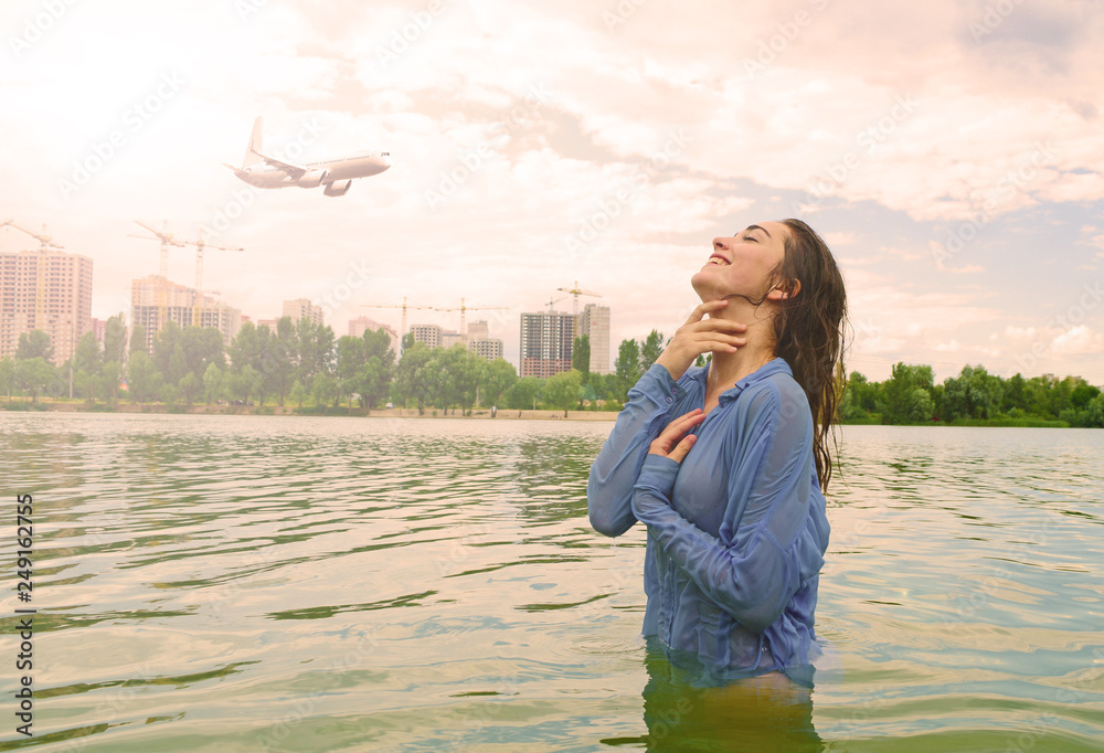 Wet erotic girl in a shirt on the lake. In the sky the plane flies and the sun shines.