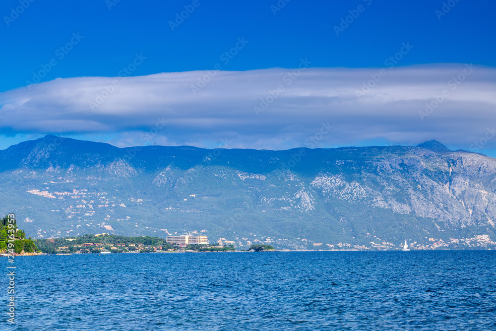 Wonderful romantic summertime panoramic seascape. Sailing yacht with white sails in to the crystal clear azure sea. Small green island against coastline slopes.