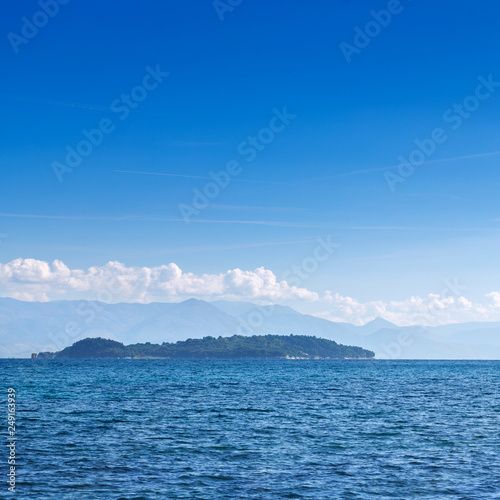 Wonderful romantic summertime panoramic seascape. Sailing yacht with white sails in to the crystal clear azure sea. Small green island against coastline slopes.