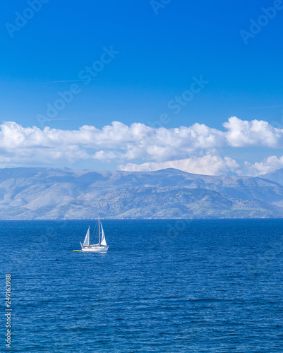 Wonderful romantic summertime seascape. Sailing yacht with white sails in to the crystal clear azure sea against coastline slopes.