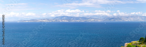 Wonderful romantic summertime panoramic seascape. Sailing yacht with white sails in to the crystal clear azure sea against coastline slopes.