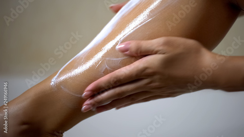 Female hands applying moisturizing body lotion on leg after depilation, hygiene photo