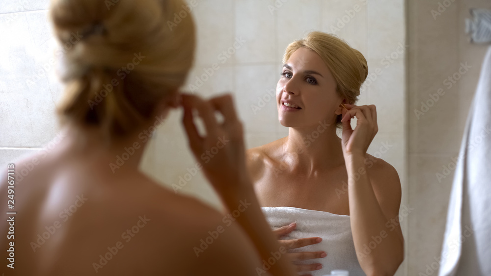 Young woman cleaning ears with cotton swab in bathroom, morning procedure health
