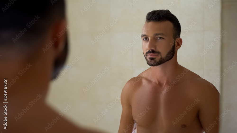 Bearded handsome man looking in mirror, perfect body, daily workout result
