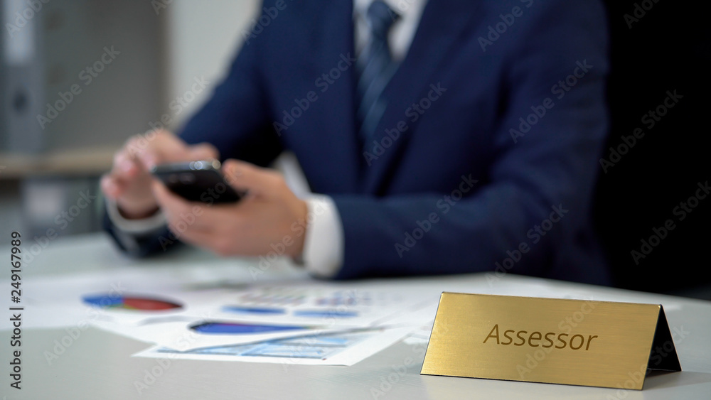 Male assessor in business suit using smartphone, working on important documents Male assessor in business suit using smartphone, working on important documents