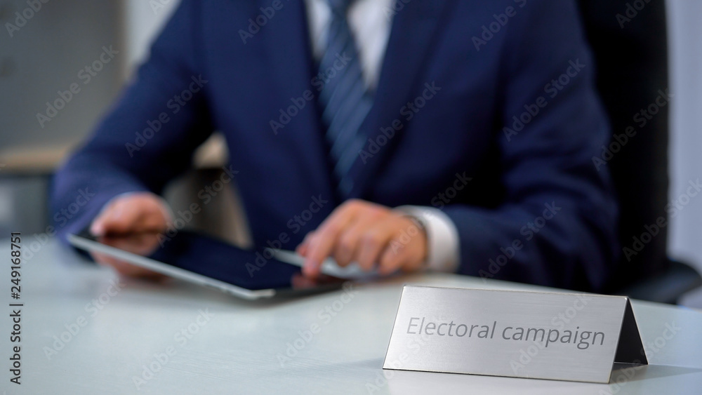 Serious politician working on tablet pc, preparing program for election campaign Serious politician working on tablet pc, preparing program for election campaign