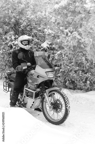 Rider man is sitting on adventure motorcycle. Winter fun. snowy day. motorbike and snow. black and white. off road dual sport travel tour  active life style concept. winter clothes  vertical photo