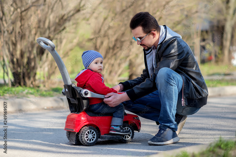 Little toddler boy sitting on red push car and listening to his father explaining him traffic law and safety rules. Father and son conversation Little toddler boy sitting on red push car and listening to his father explaining him traffic law and safety rules. Father and son conversation