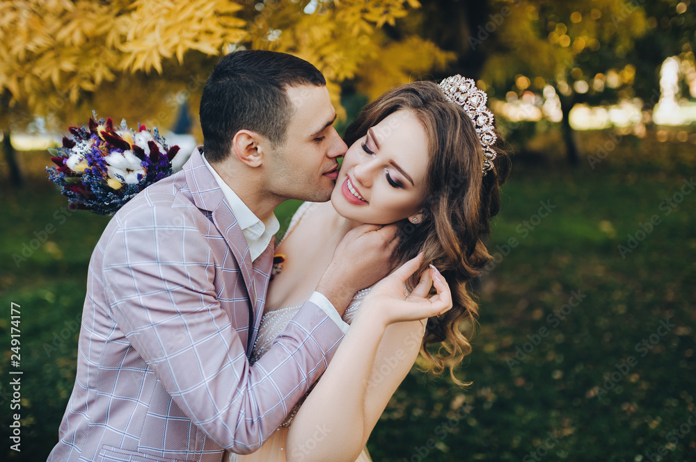 Newlyweds in love embrace in the fall in the park with yellow foliage. Stylish groom in a plaid jacket kisses a pretty bride in a beige dress with a crown. Wedding photography. Princess Bride Newlyweds in love embrace in the fall in the park with yellow foliage. Stylish groom in a plaid jacket kisses a pretty bride in a beige dress with a crown. Wedding photography. Princess Bride