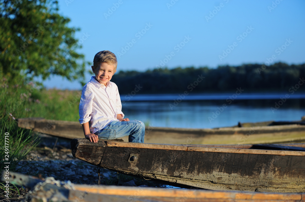 A small smiling four year old boy is sitting on a boat by the river A small smiling four year old boy is sitting on a boat by the river