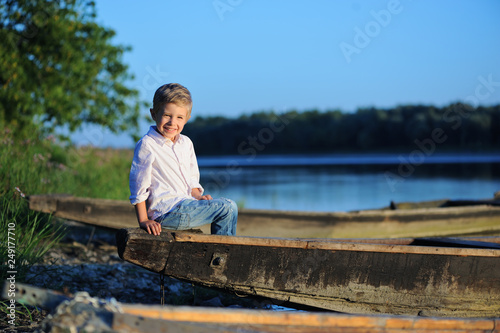 A small smiling four year old boy is sitting on a boat by the river