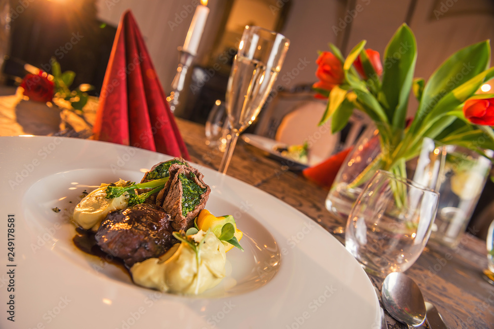 baked beef with baby patizone, sauce and spinach served on white plate with flowers and champagne, romantic time on valentines day baked beef with baby patizone, sauce and spinach served on white plate with flowers and champagne, romantic time on valentines day
