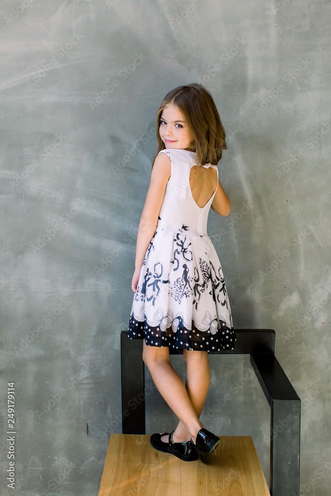 Fototapeta premium Cute little girl in white dress smiling on camera with long hair