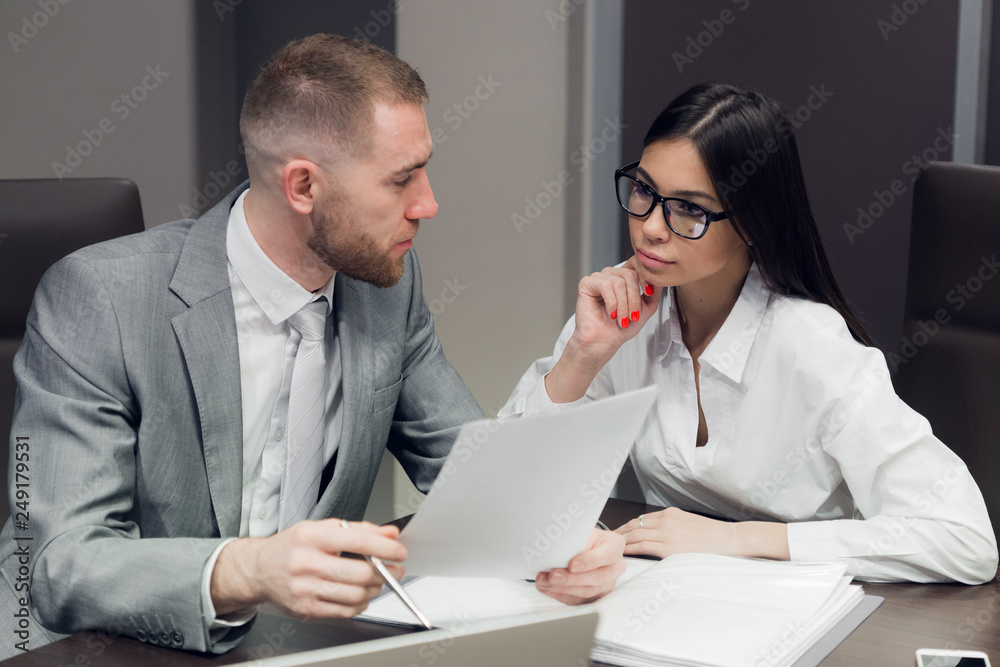 Two young business people discussing work during a business presentation in conference room Two young business people discussing work during a business presentation in conference room