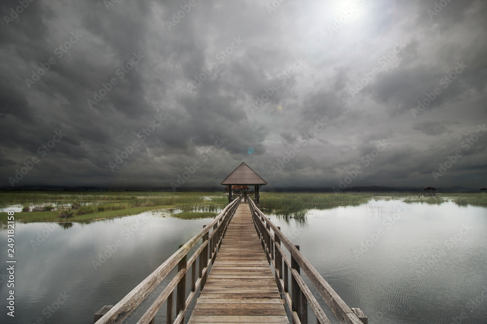 Wooden walkway place in wetland.Sky is cover by rains clouds.The wooden path connect to wooden pavilion.(Location : Khao Sam Roi Yot,Prachuap Khiri khan,Thailand)