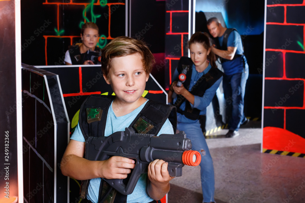 Foto Stock Excited boy aiming laser gun at other players during laser tag  game in dark room