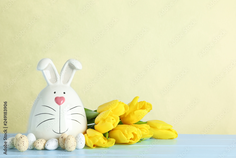 Fototapeta premium Decorated bunny and Easter eggs on table against color background. Space for text