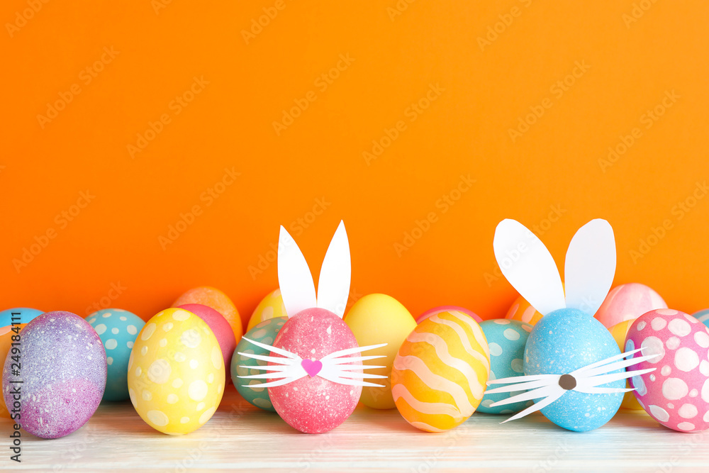 Decorated Easter eggs and cute bunny's ears on table against color background. Space for text Decorated Easter eggs and cute bunny's ears on table against color background. Space for text