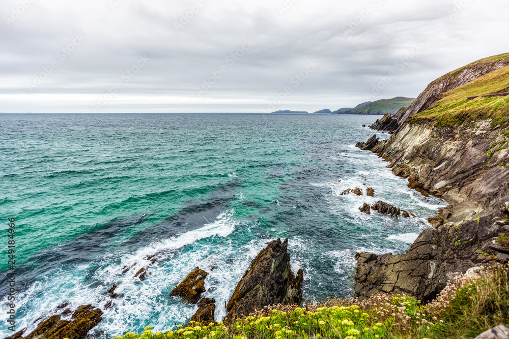 View from cliff towards rocky coastline, sea waves, cliffs and islands in the distance, moody stormy clouds