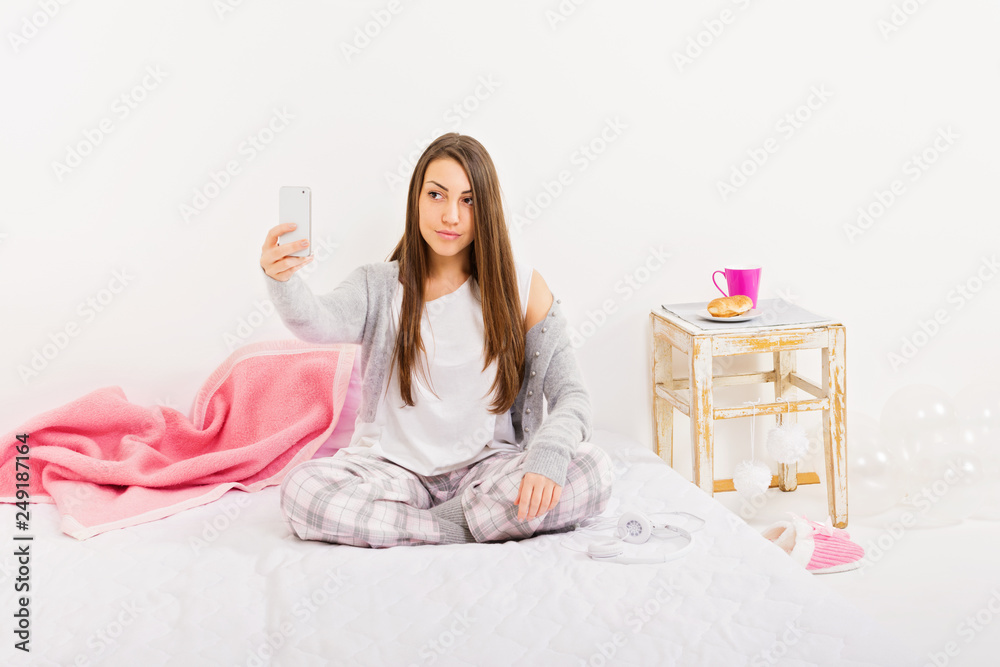 Teenage girl in pajamas, posing, taking a selfie on smartphone in her modern  minimalist pastel colored bedroom at home in the morning. No retouch.  Natural and studio lighting. Stock Photo | Adobe