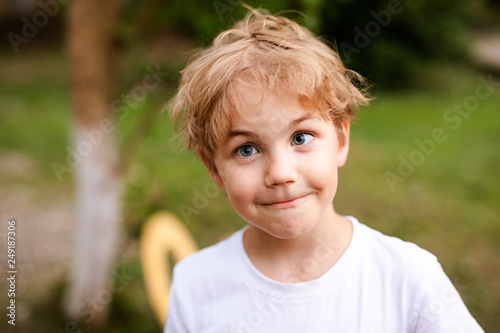 Blonde smiling boy with strabismus in warm park