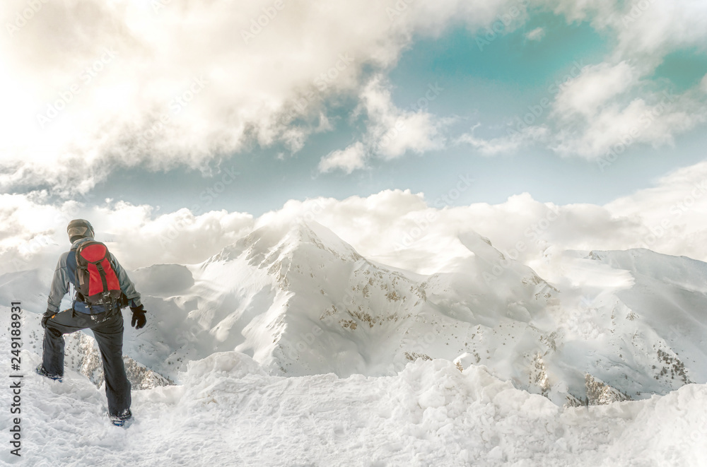 Snowboarder stay with snowboard in hands sits on big rock on mountains backdrop. Bansko, Bulgaria Snowboarder stay with snowboard in hands sits on big rock on mountains backdrop. Bansko, Bulgaria