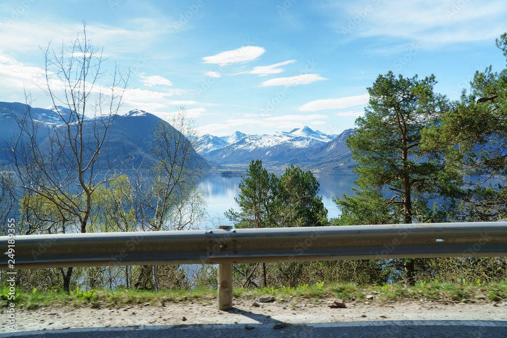 Norwegian spring landscape, view from road side near fjord, scenic mountains and blue sky at background.