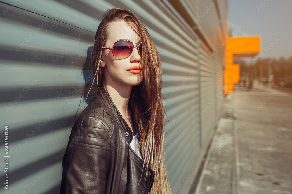 Young fashionable girl near shopping center in sun glasses smiling and positive. Orange and grey background Young fashionable girl near shopping center in sun glasses smiling and positive. Orange and grey background