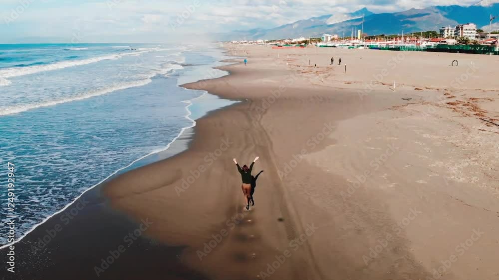 Aerail drone, Girl tourist runs along beach viareggio italy wave line in jeans. Freedom concept.
