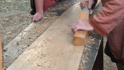 Carpenter in Medieval Cotton Clothes Working With a Wood by Plane. Man Manually Hews a Wooden Board With a Plane photo