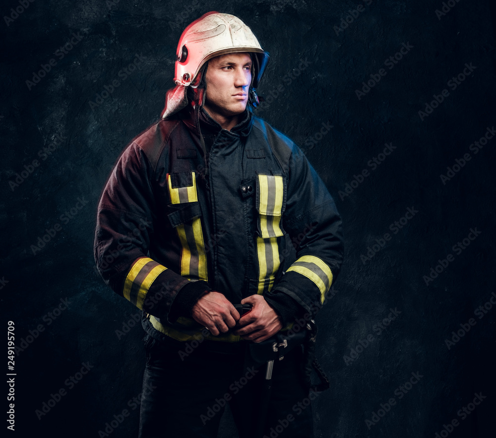 Fototapeta premium Studio portrait of firefighter dressed in uniform and safety helmet looking sideways with a confident look