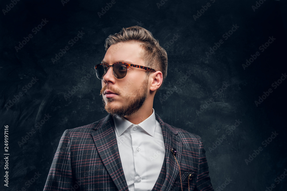 An elegantly dressed young man in sunglasses against a dark textured wall An elegantly dressed young man in sunglasses against a dark textured wall
