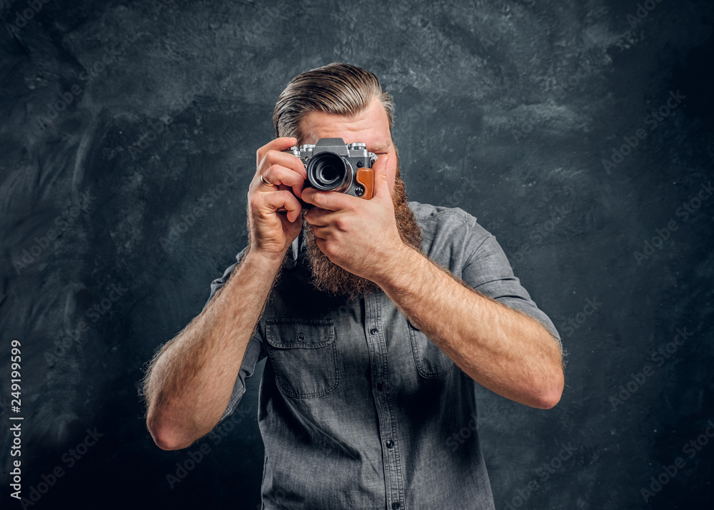 A bearded photographer wearing a gray shirt takes a photo. Studio shot on a gray textured wall A bearded photographer wearing a gray shirt takes a photo. Studio shot on a gray textured wall