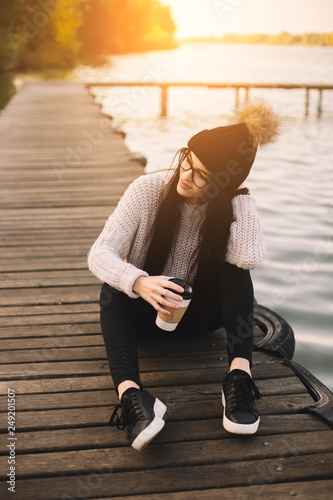 Young woman in glasses with cup of coffee on river pier