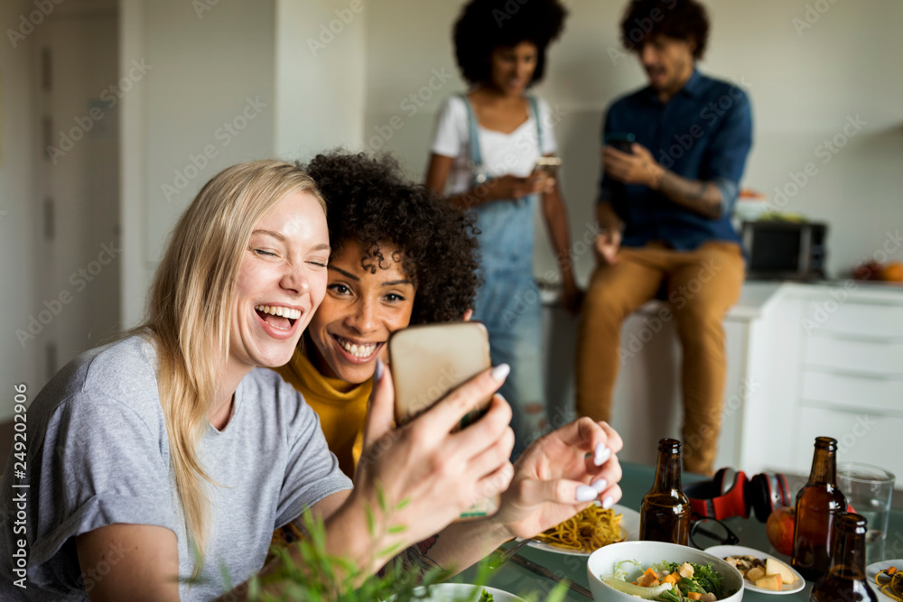 Happy girlfriends with cell phone sitting at dining table Happy girlfriends with cell phone sitting at dining table