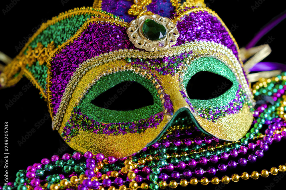 Jester carnival mask with beads in foreground on a black background.