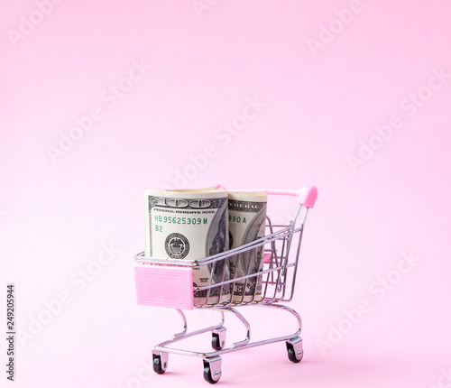 Supermarket Cart Full of US Dollar banknotes on a pink background with Copy Space. Free trade. money market. Minimalism style. Shop trolley at supermarket. Sale, discount