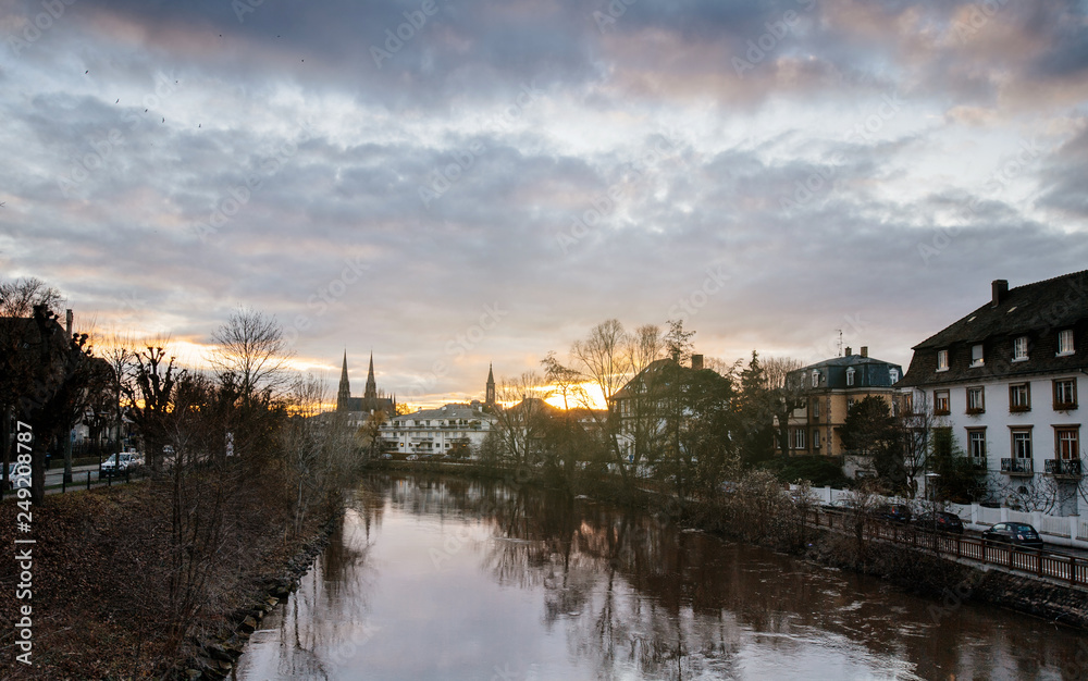 Strasbourg sunset with cloudy and sunny sky with Reformed Church Saint Paul and Ill river, cars parked and houses