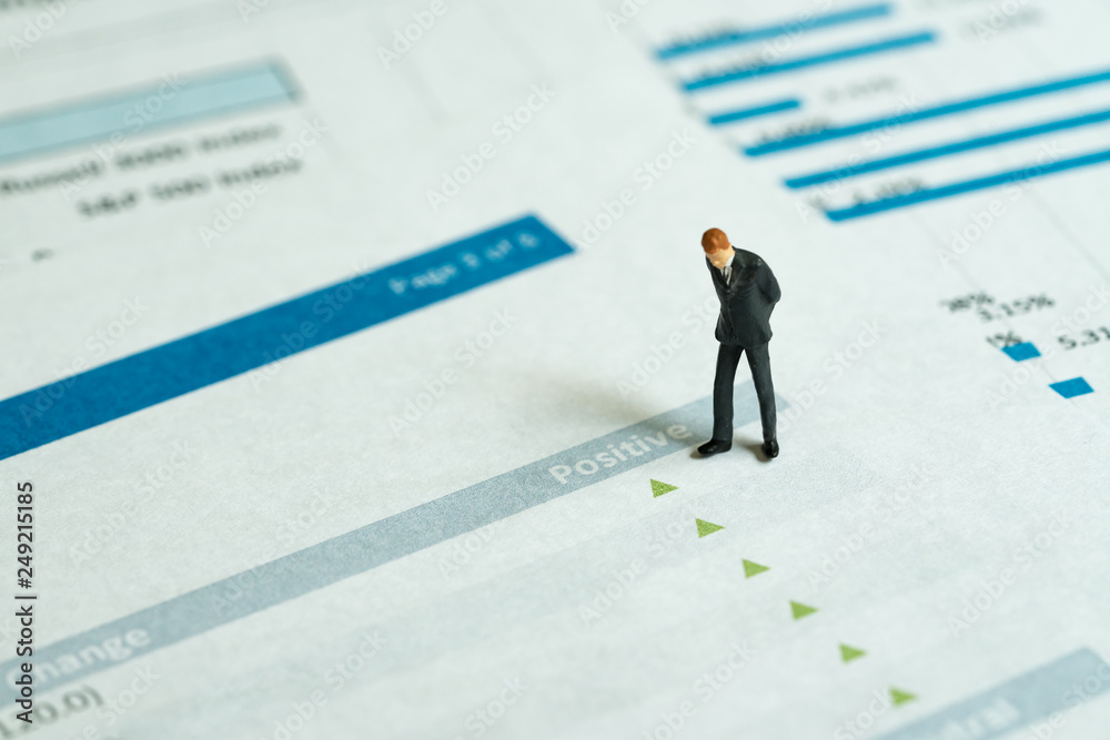 Miniature businessman looking at green pointing up arrows of investment report, stock price go up, positive sentiment, good sign of situations in which some financial assets gain value Miniature businessman looking at green pointing up arrows of investment report, stock price go up, positive sentiment, good sign of situations in which some financial assets gain value